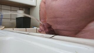 Naked mature man peeing in sink.